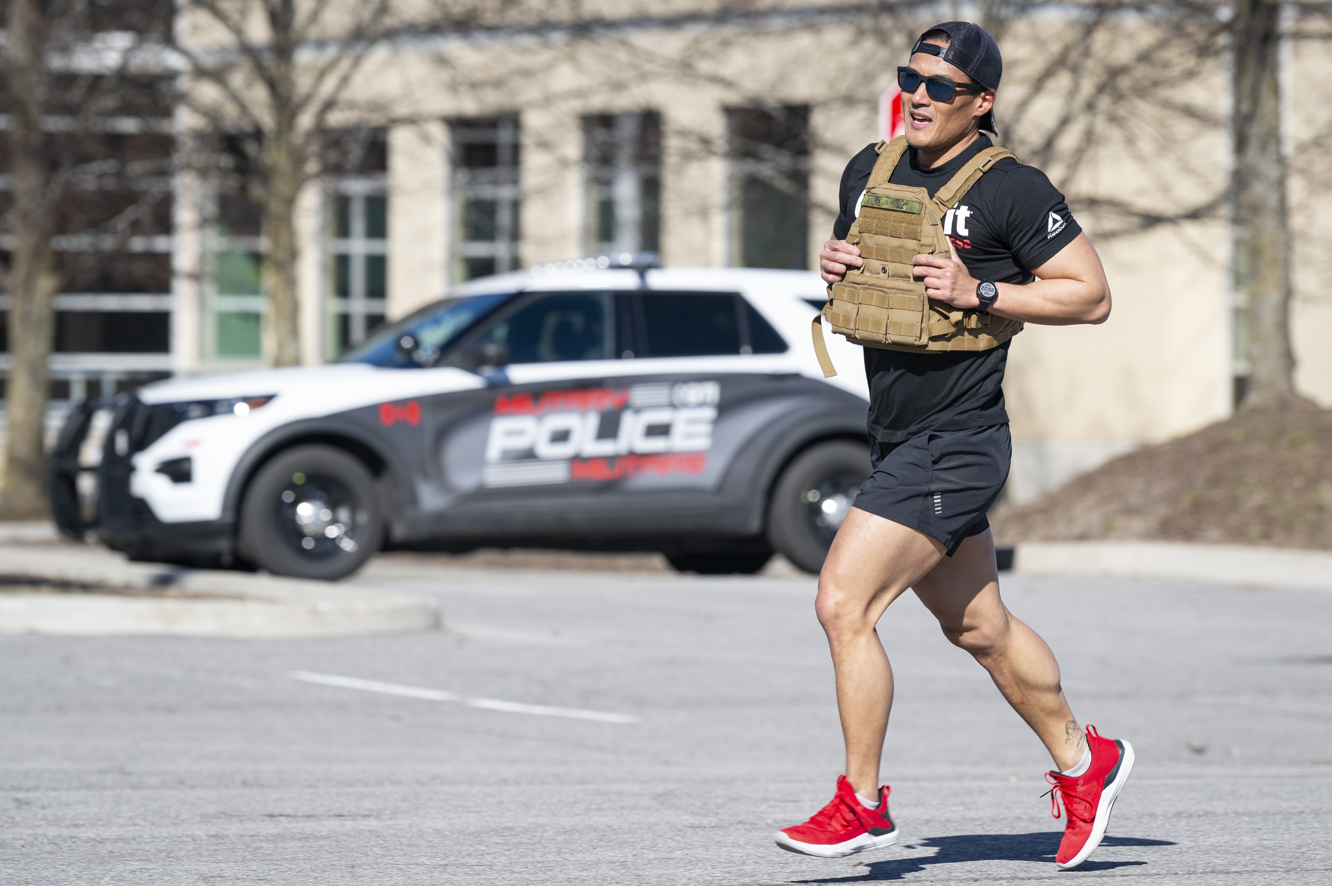 A member of the Military Police, dressed in shorts and a t-shirt wearing a ballistic plate vest,
runs in front of a military police vehicle in the background.